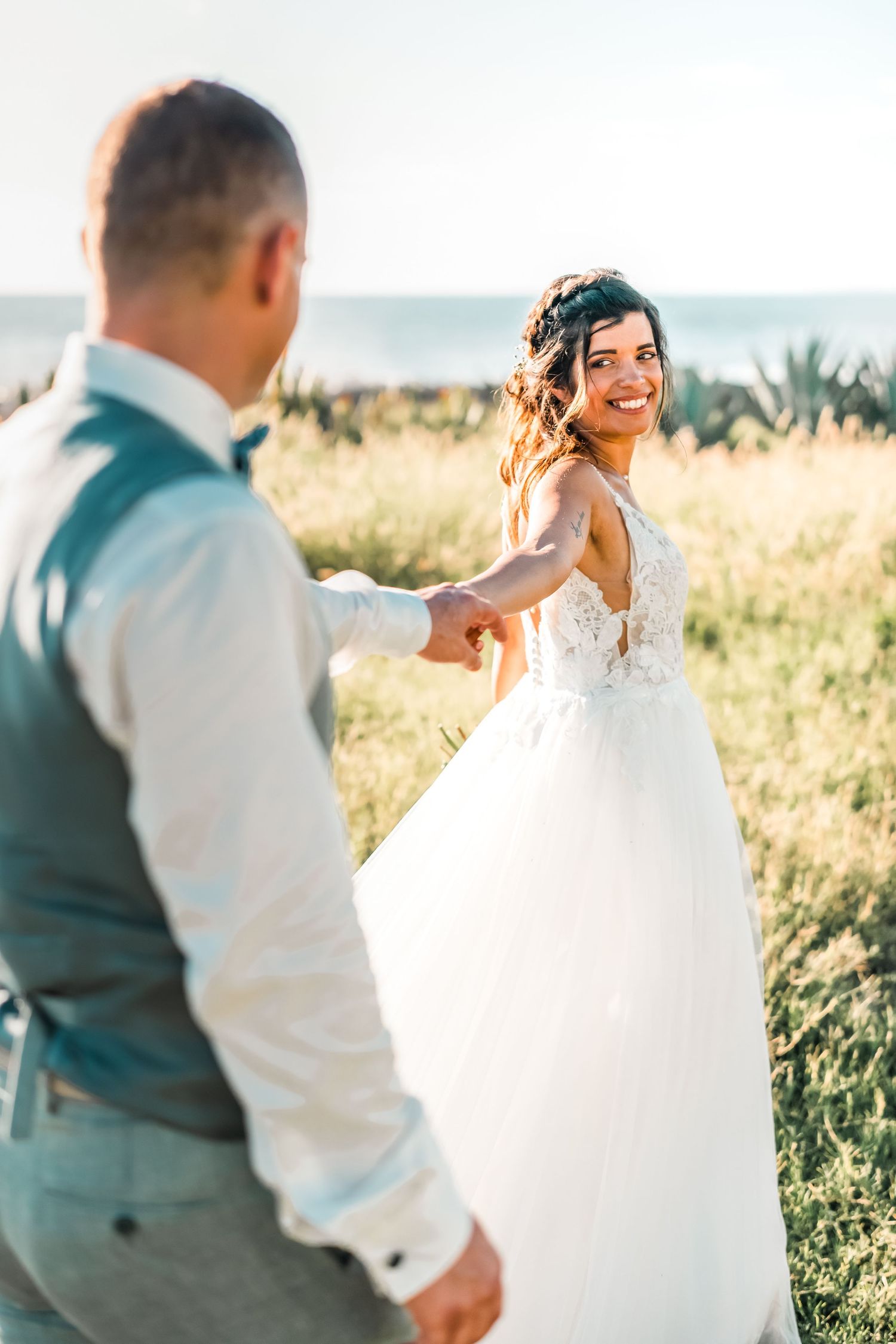 A romantic couple dances together in a sun-lit field during a wedding photoshoot at golden hour.