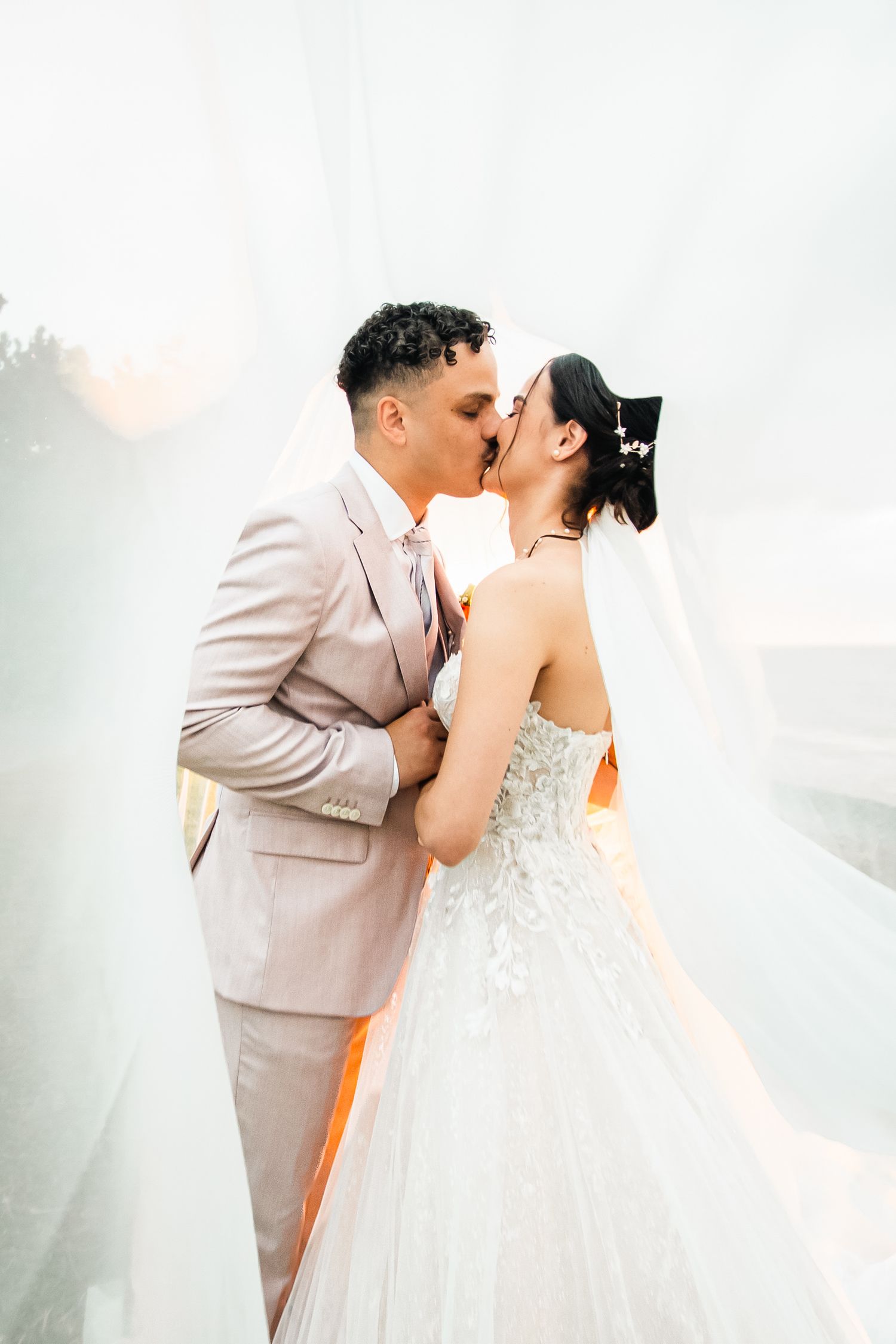 A romantic wedding couple shares a tender kiss in a dreamy outdoor setting with soft lighting and mist.