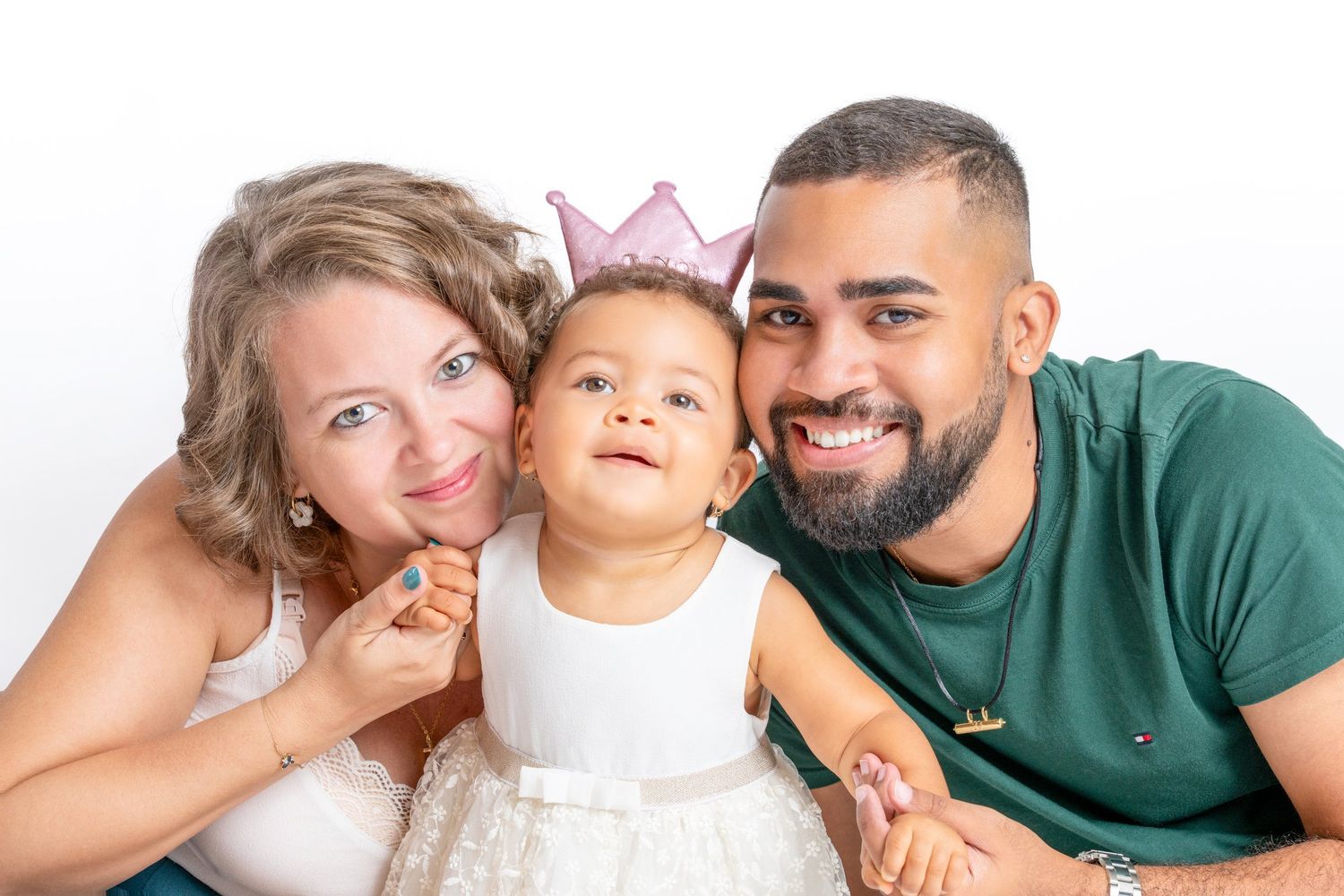 A happy family portrait with a smiling couple and their baby girl wearing a pink crown on a white background.