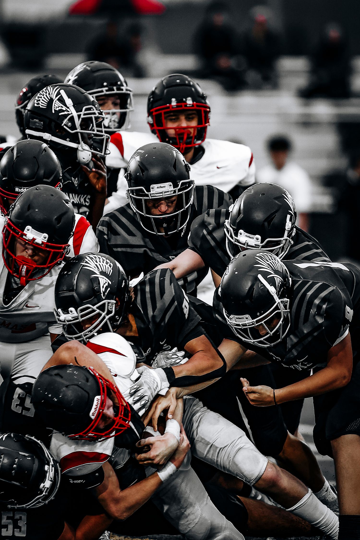 Football players in black and red uniforms collide in an intense tackle during a game.