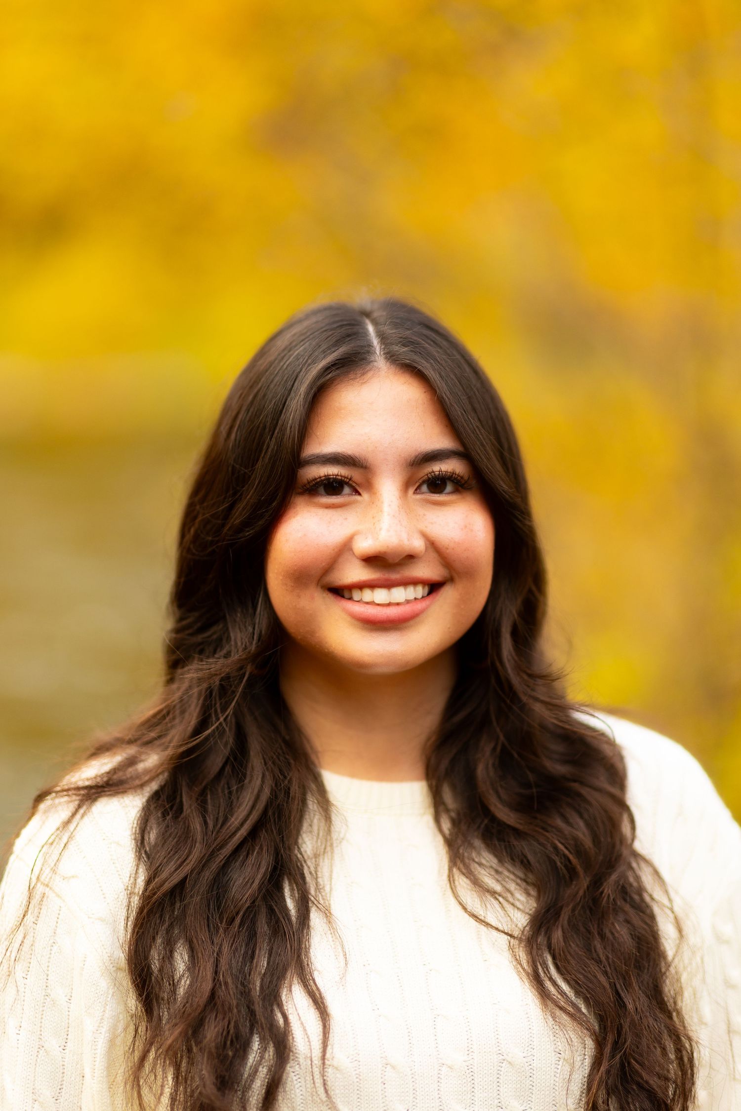 Portrait of woman in white sweater against blurred yellow autumn background.
