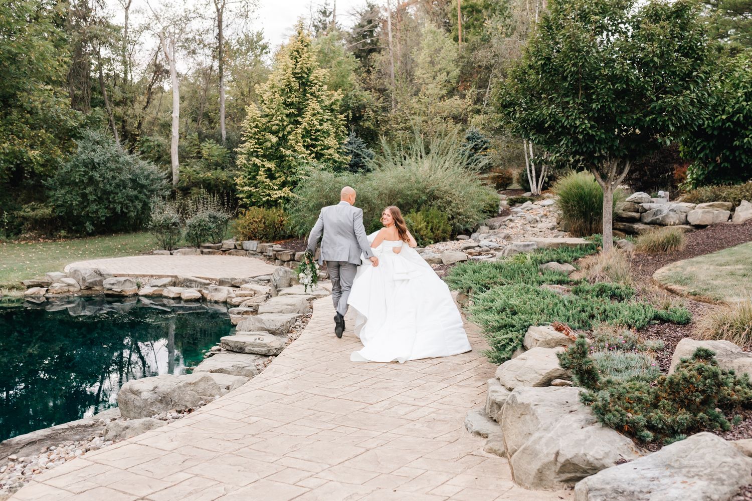 Wedding couple walking along stone path beside tranquil garden pond. Pittsburgh wedding Photographer