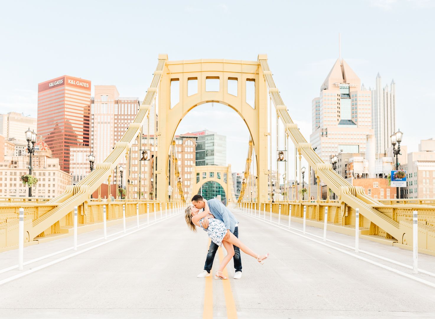Couple sharing romantic pose on Pittsburgh's iconic yellow bridge with city skyline backdrop.