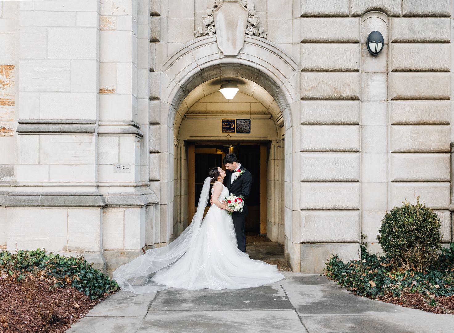 Bride and groom pose under stone archway entrance of historic building. Pittsburgh wedding Photographer