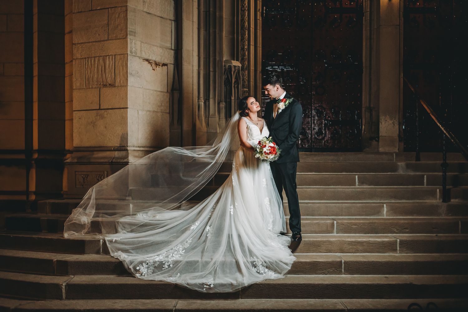 Dramatic wedding portrait on church steps with bride's flowing veil in evening light. Pittsburgh wedding Photographer