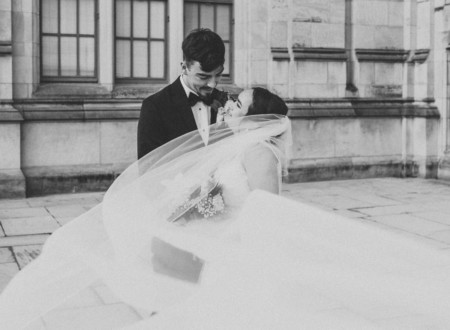Black and white photo of a romantic wedding couple with flowing veil against stone architecture. Pittsburgh wedding Photographer