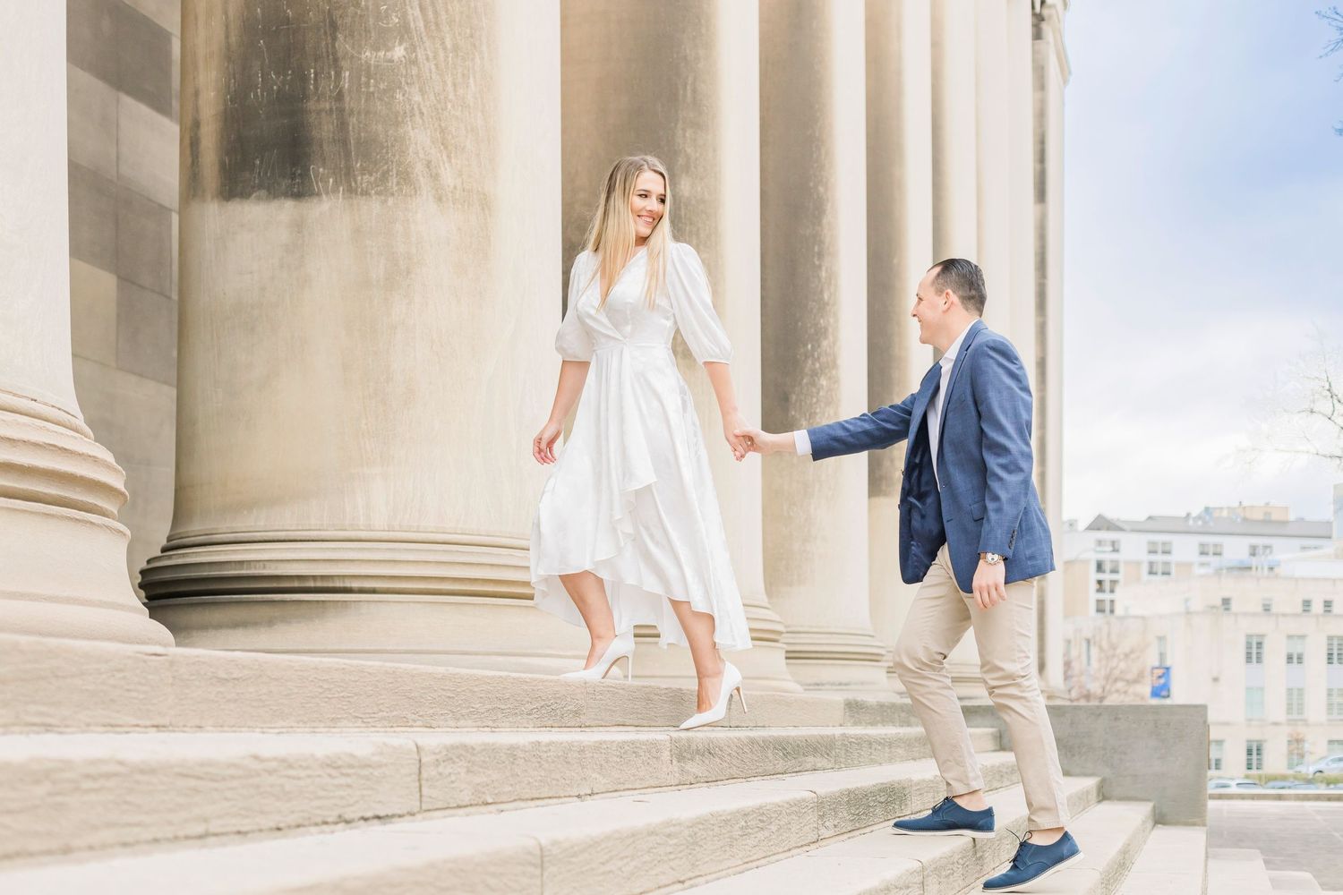 A couple descends grand marble steps at a historic building entrance.