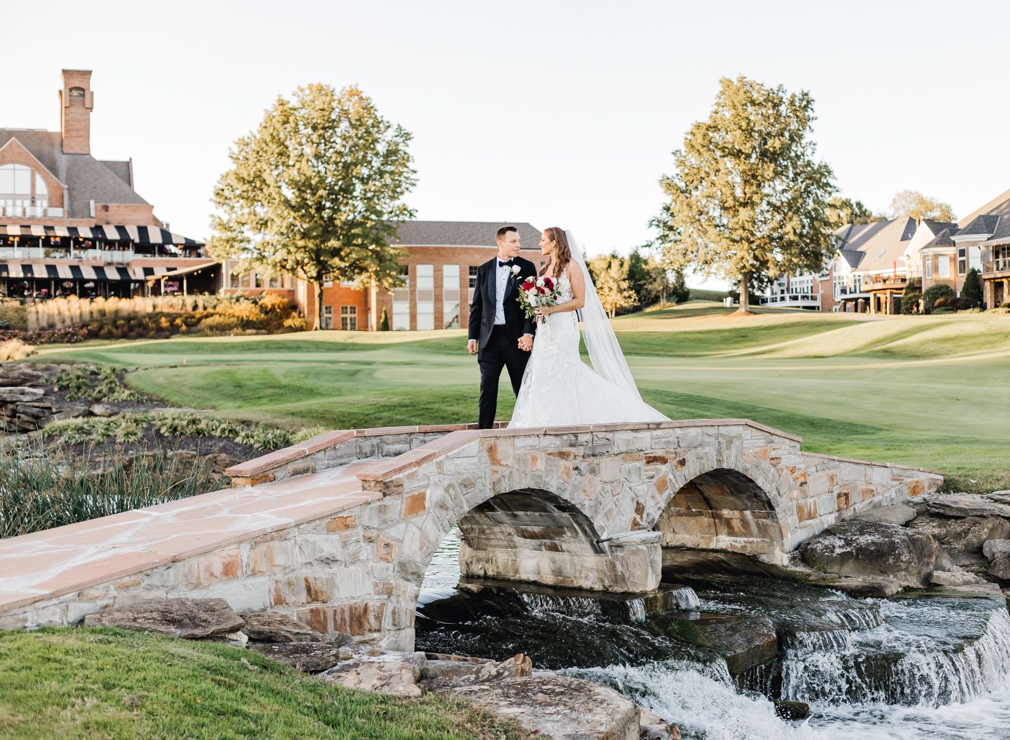Wedding couple posing on rustic stone bridge with classic clubhouse in background. Pittsburgh wedding Photographer