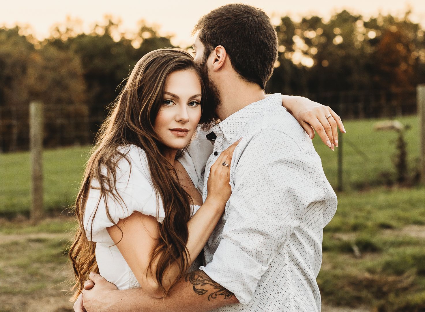 A romantic countryside engagement photo during golden hour in a rustic setting.
