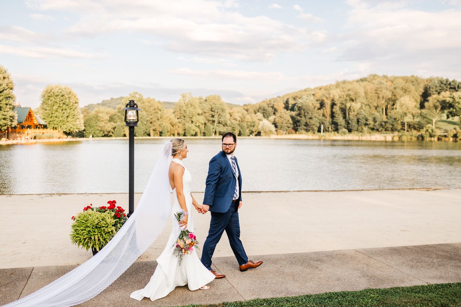 Wedding couple walking along lakeside path with flowing white dress and autumn trees. Pittsburgh wedding Photographer
