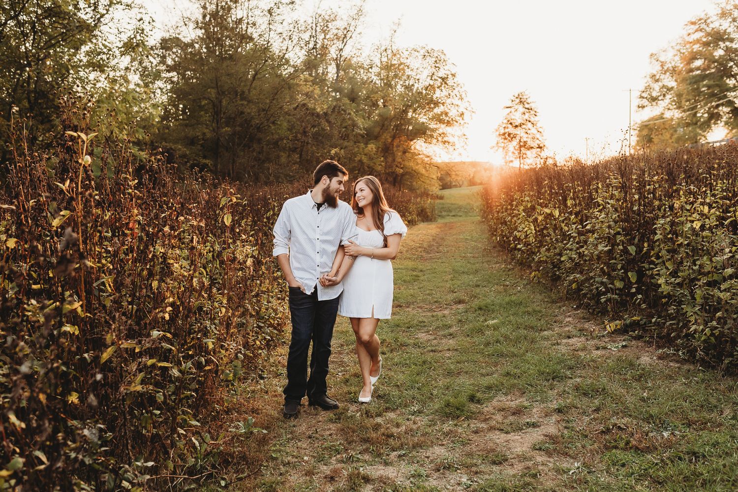 Couple walking together during golden hour in a rustic field setting.