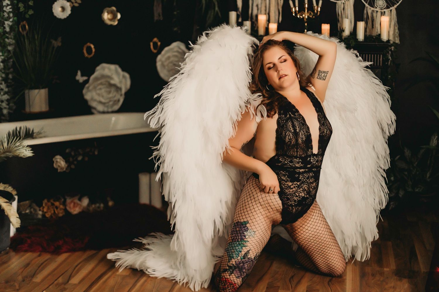Boudoir photo with large white angel wings and lace lingerie on wooden floors.