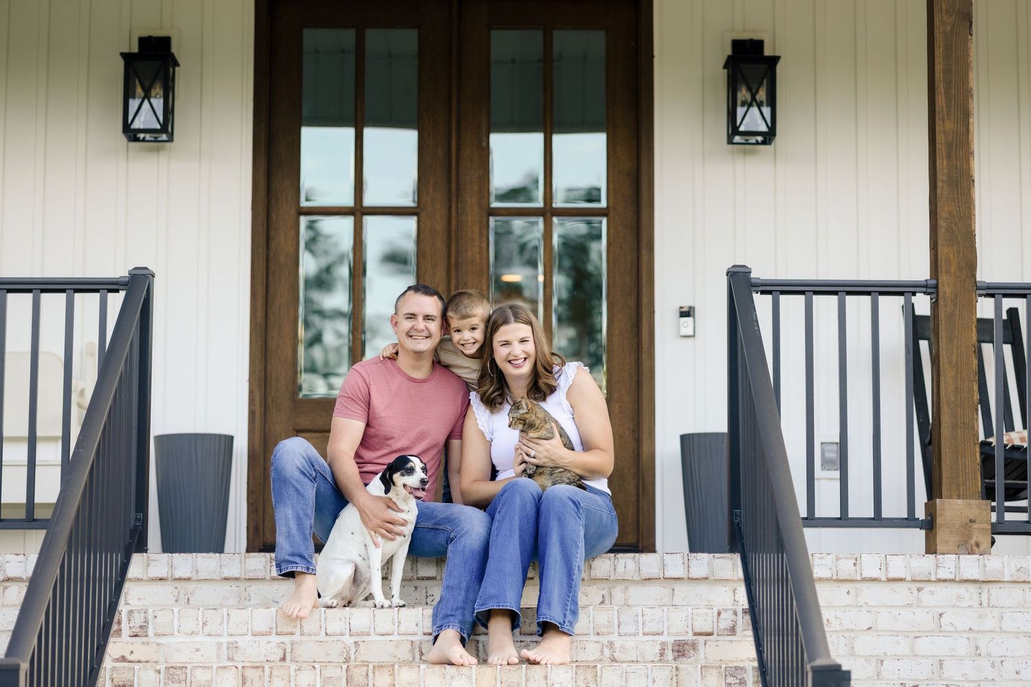 People sit and relax on a covered front porch with white brick columns and black railings.