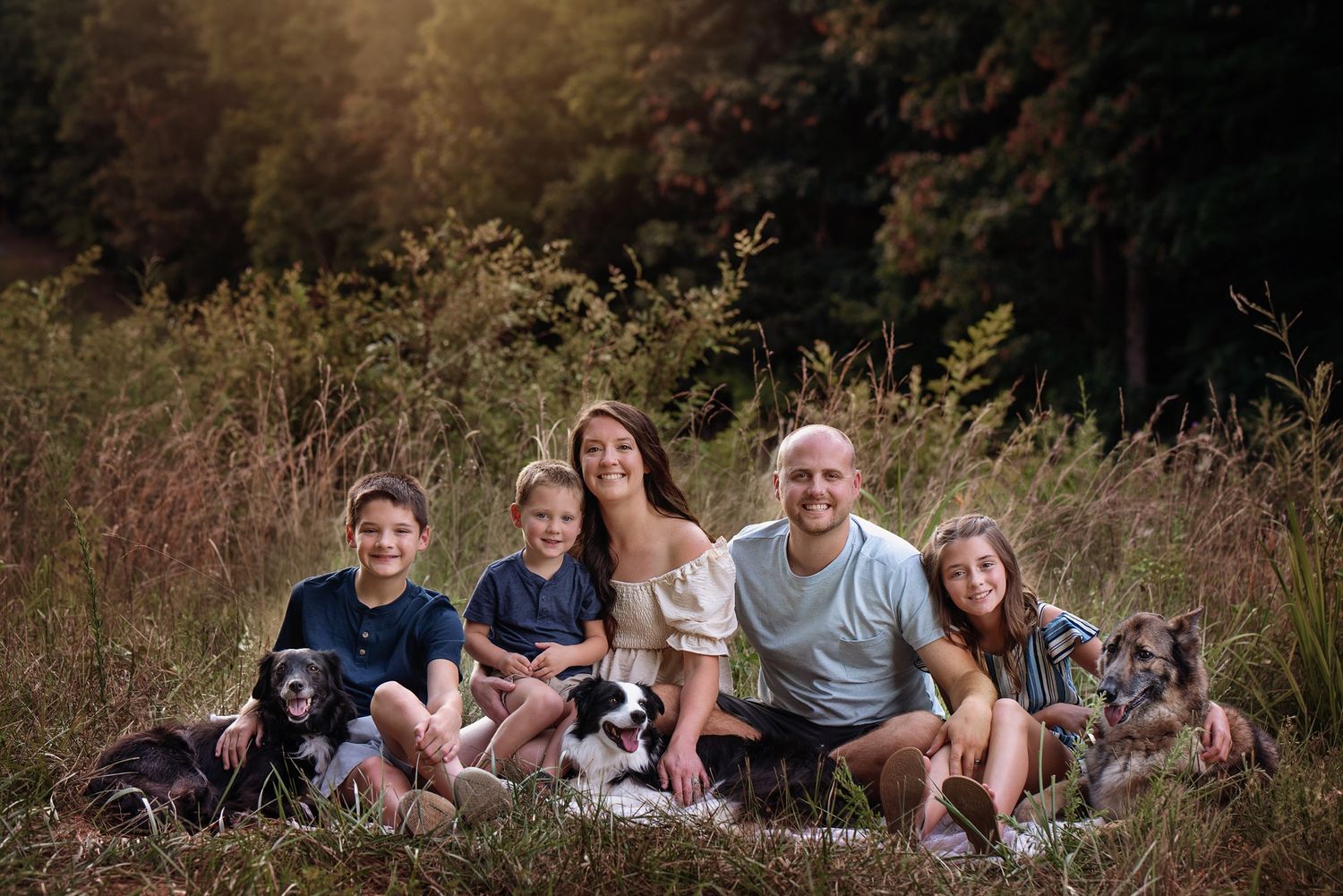 Family and their black dog pose together on grass during golden hour outdoor photo session.