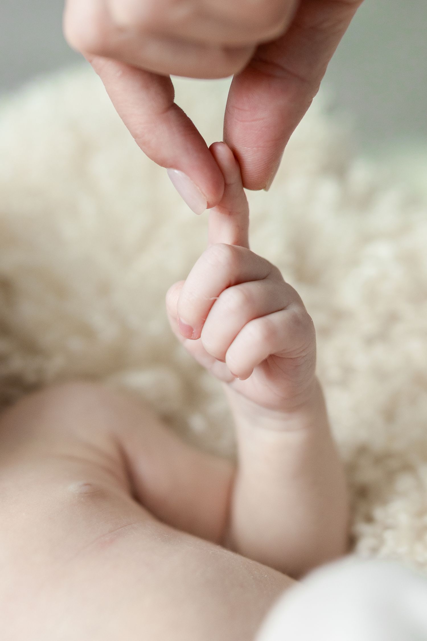 Close-up photo series showing a parent's finger gently holding a newborn baby's tiny hand on white blanket.