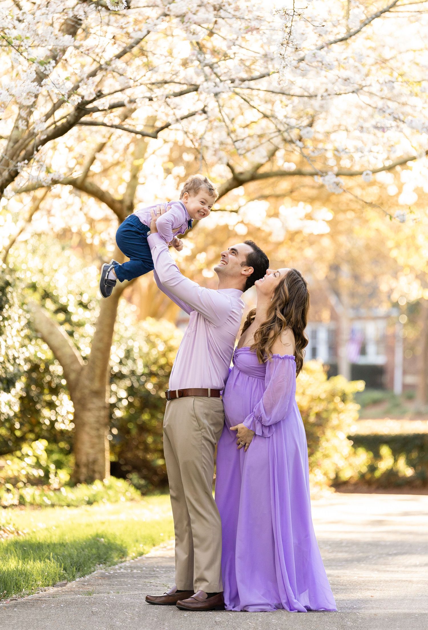Family enjoying spring cherry blossoms with playful lift under blooming trees.