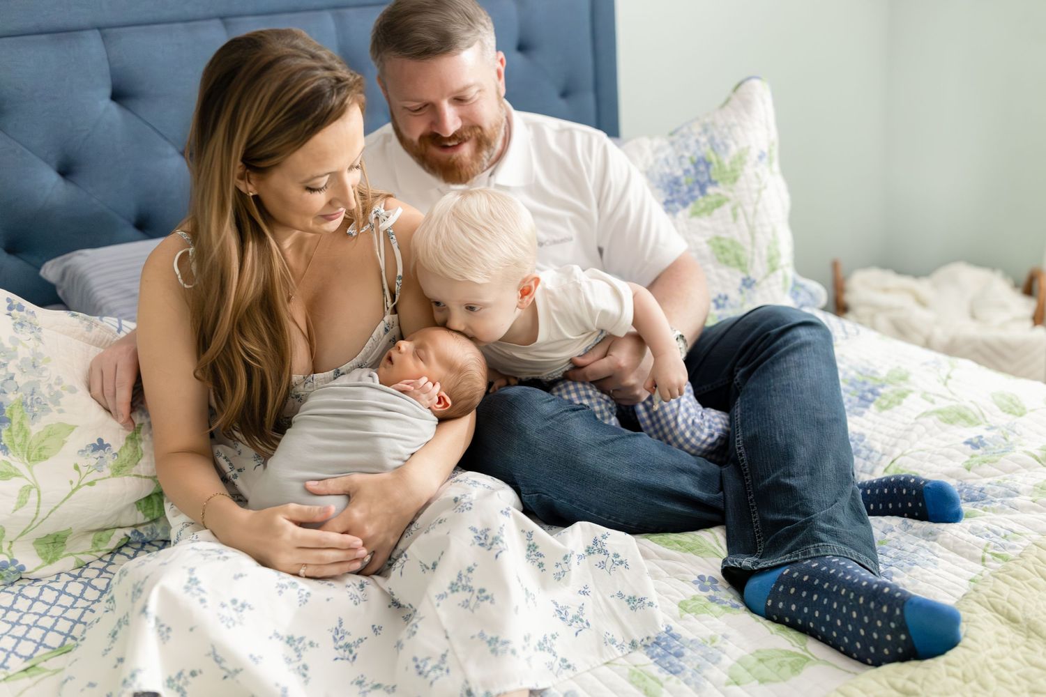 Family lounges together on floral bedding while sharing tender moments at home.