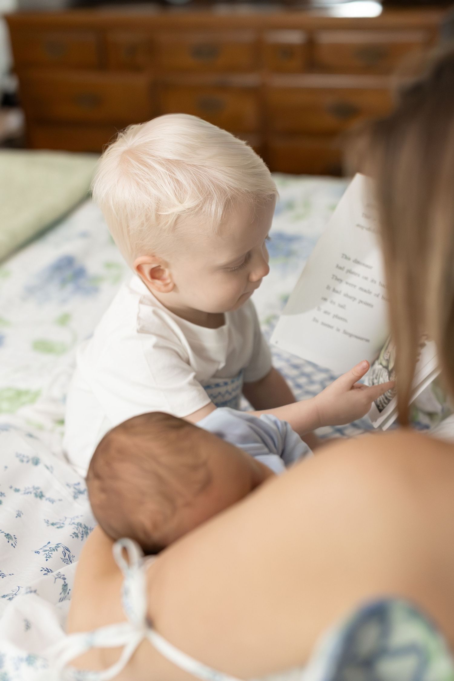A newborn baby rests on a patterned blanket while being gently held by caring hands.