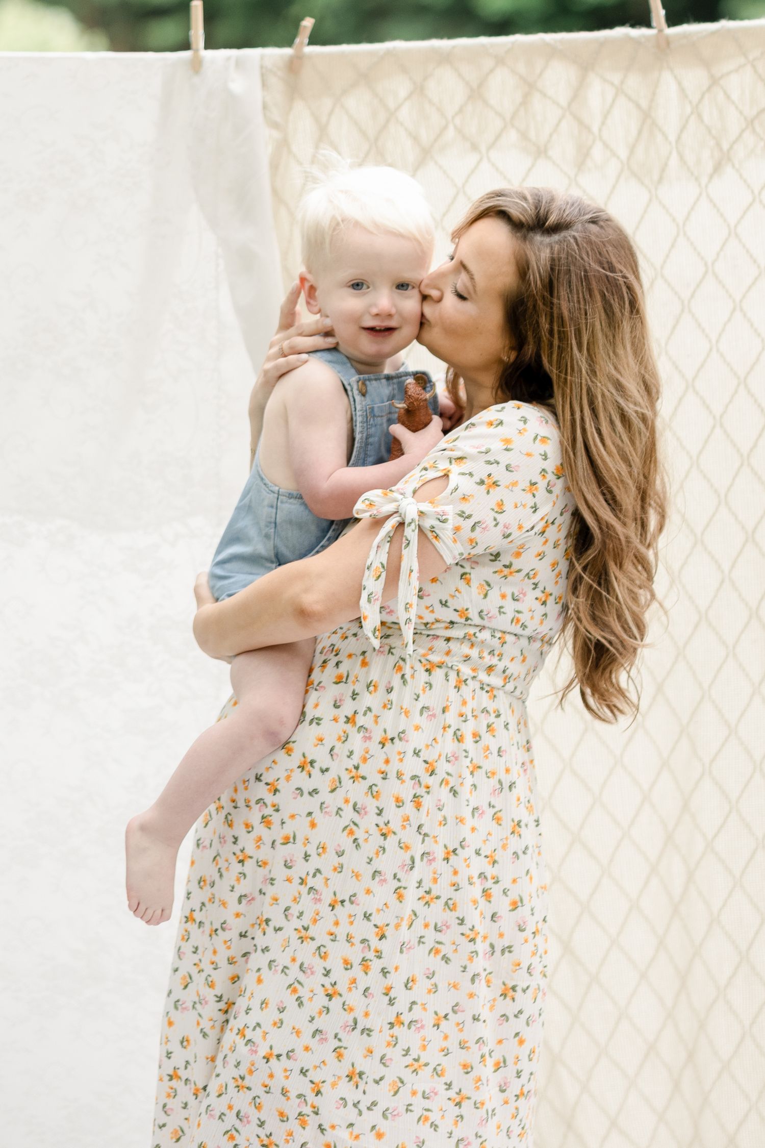 A tender moment between parent and child wearing floral dress and denim against a white lattice background.