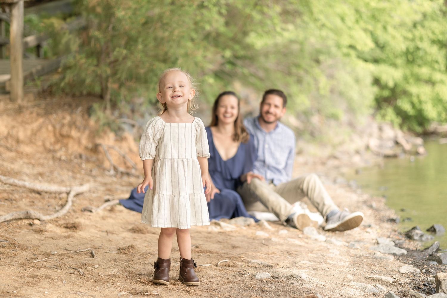 A family sits together on a fallen tree trunk near a peaceful stream in a lush forest setting.