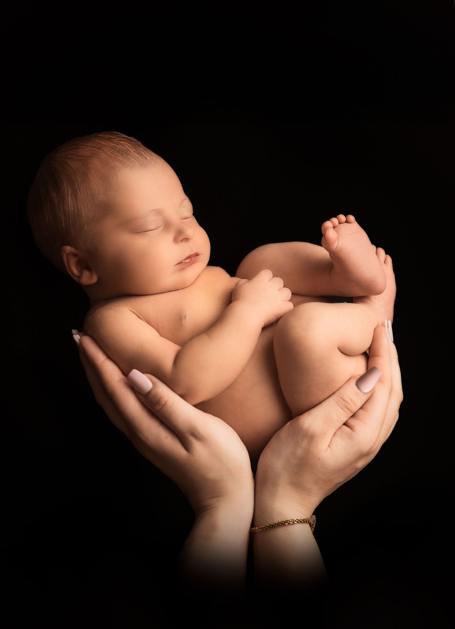 Newborn baby sleeping peacefully in cupped hands against black background, perfect newborn photography portrait.