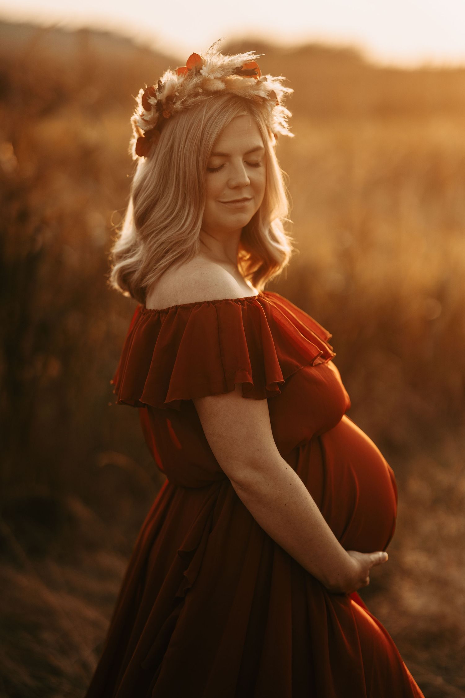A figure in a red dress with floral crown poses in a golden sunset field.