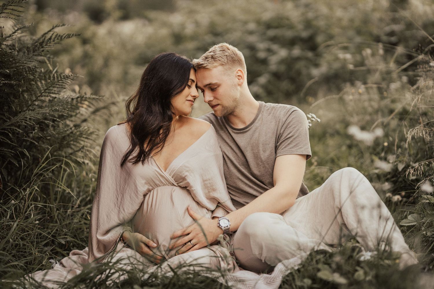 A romantic couple in neutral-toned clothing shares tender moments during an outdoor photo session in natural lighting.