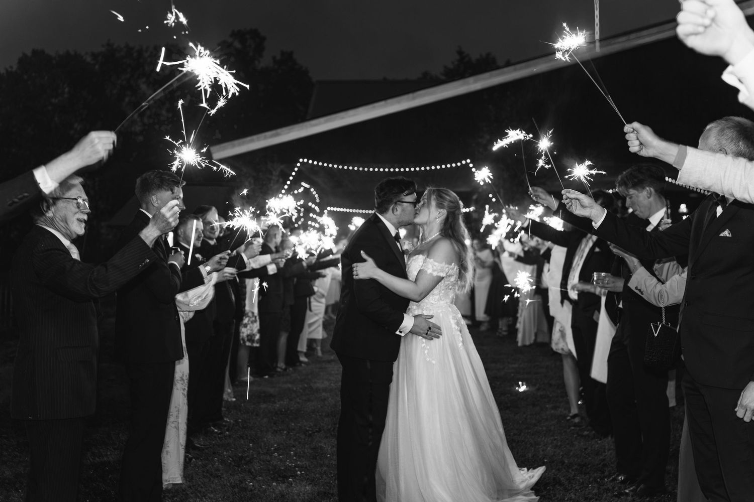 Black and white photo of a bride and groom kissing during a sparkler exit at their wedding reception.