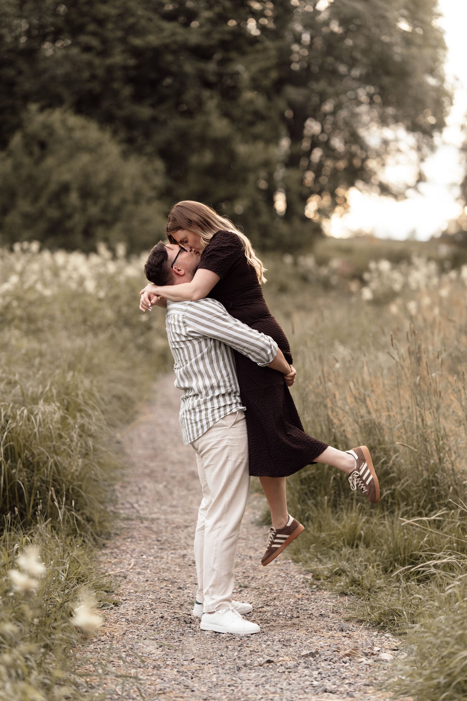 Couple sharing a romantic moment on a scenic path, man lifting woman in an embrace surrounded by lush greenery.