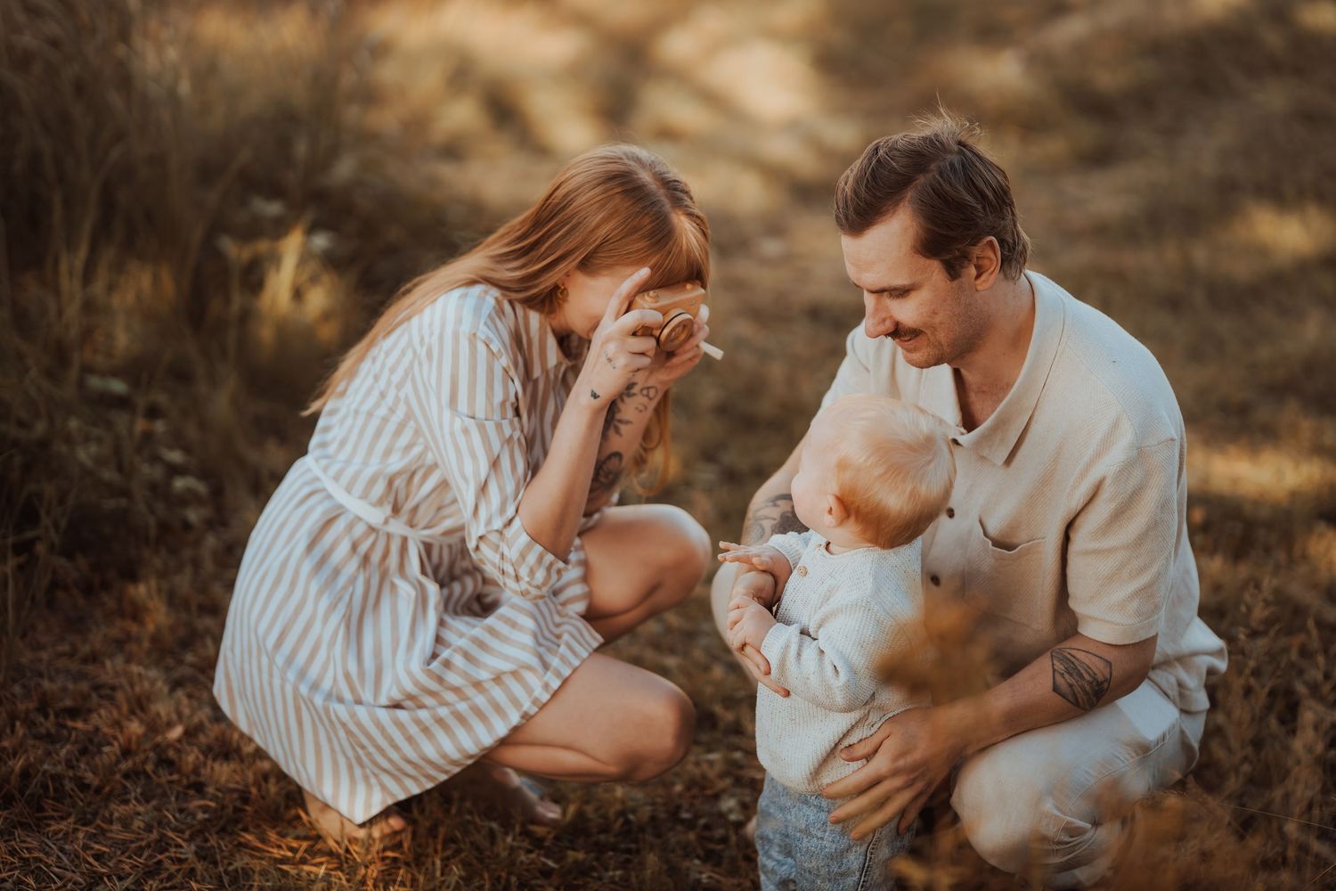 A couple in white outfits shares tender moments with their dog during a sunset photo session in a wooded setting.