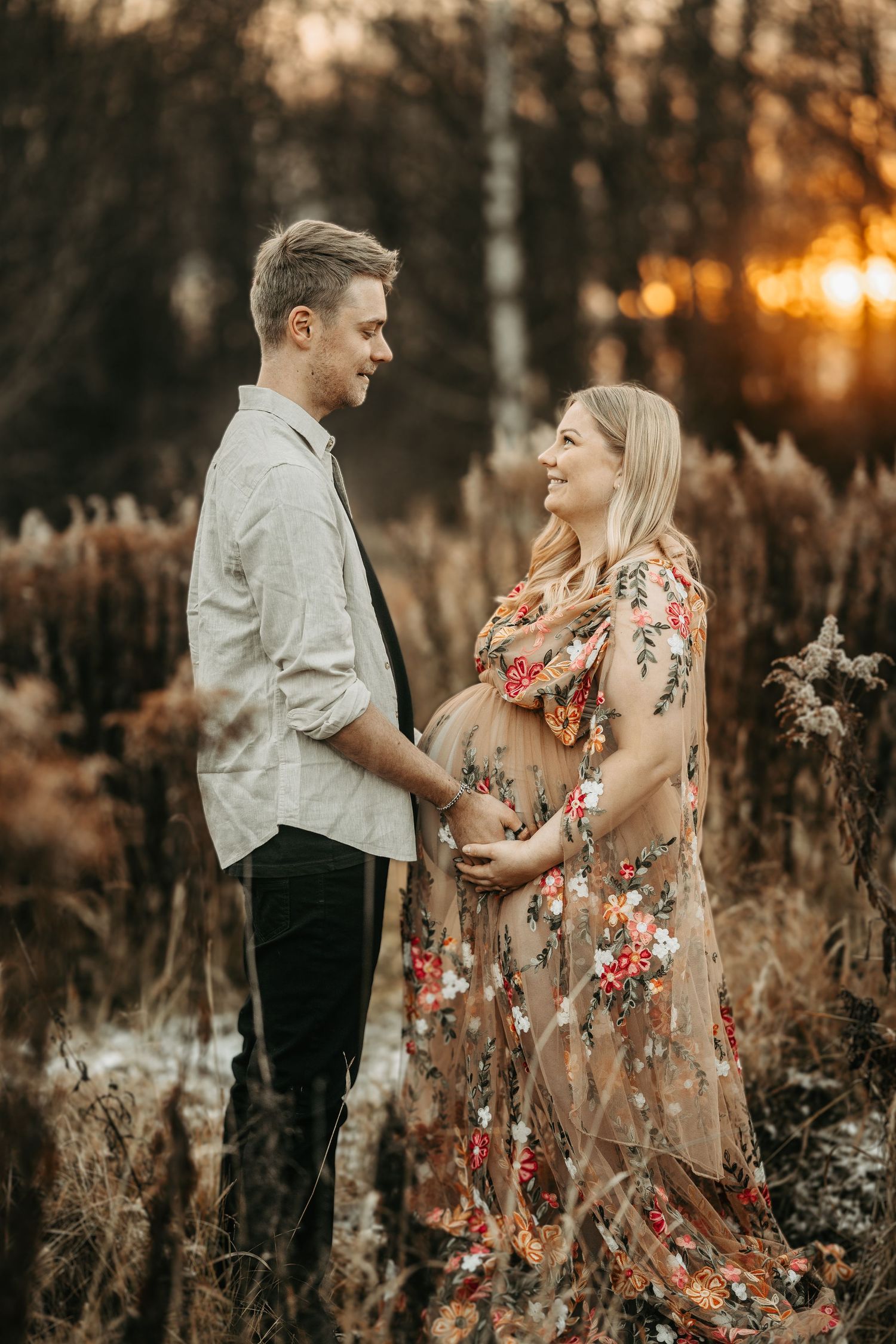 Romantic sunset maternity photo of couple in autumn field with warm golden lighting.