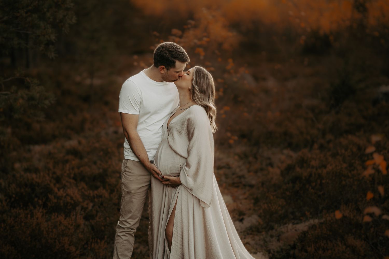 A romantic couple embraces in warm lighting against a dusky natural background.