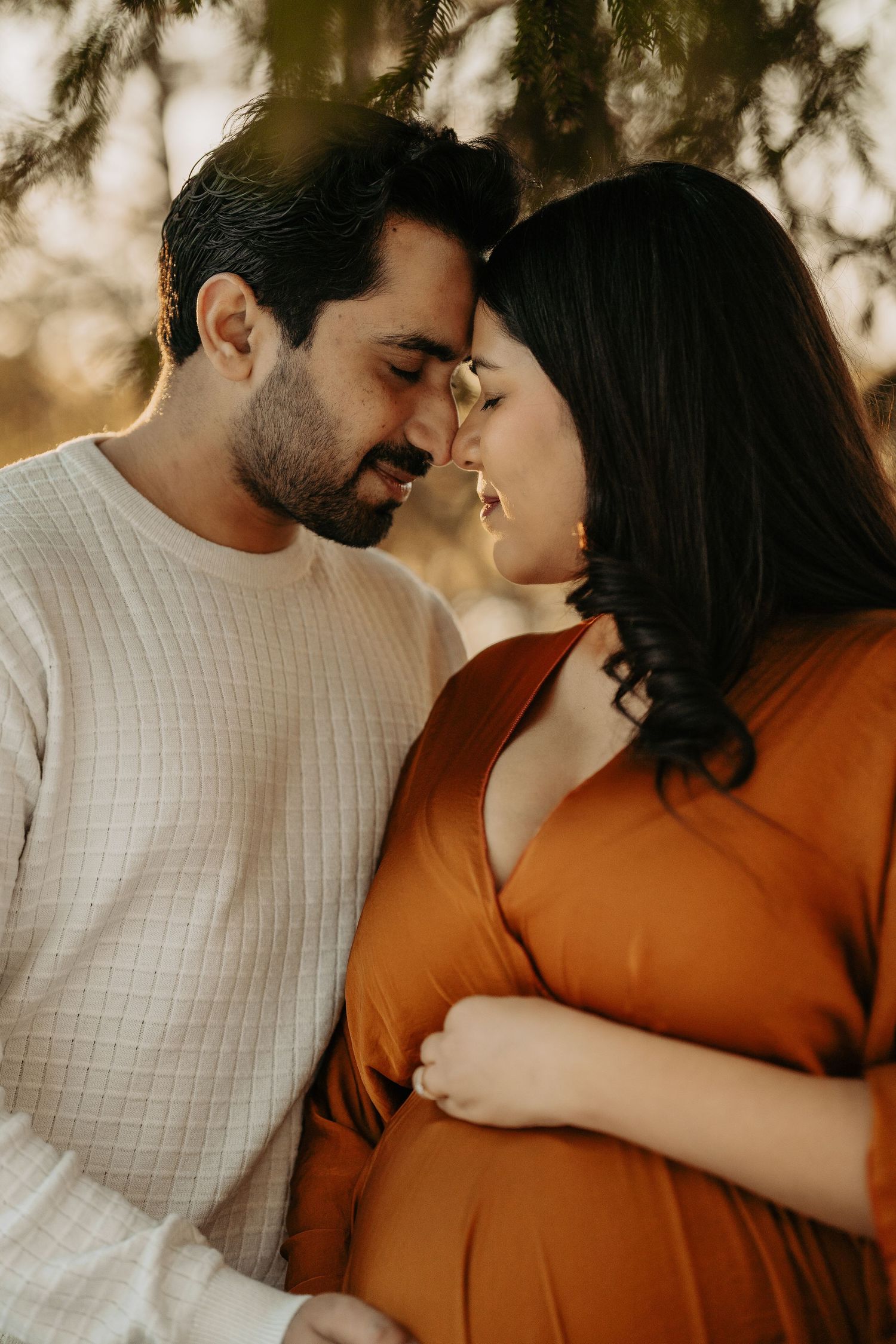 Romantic maternity portrait with couple in white and orange sharing intimate moment at sunset.