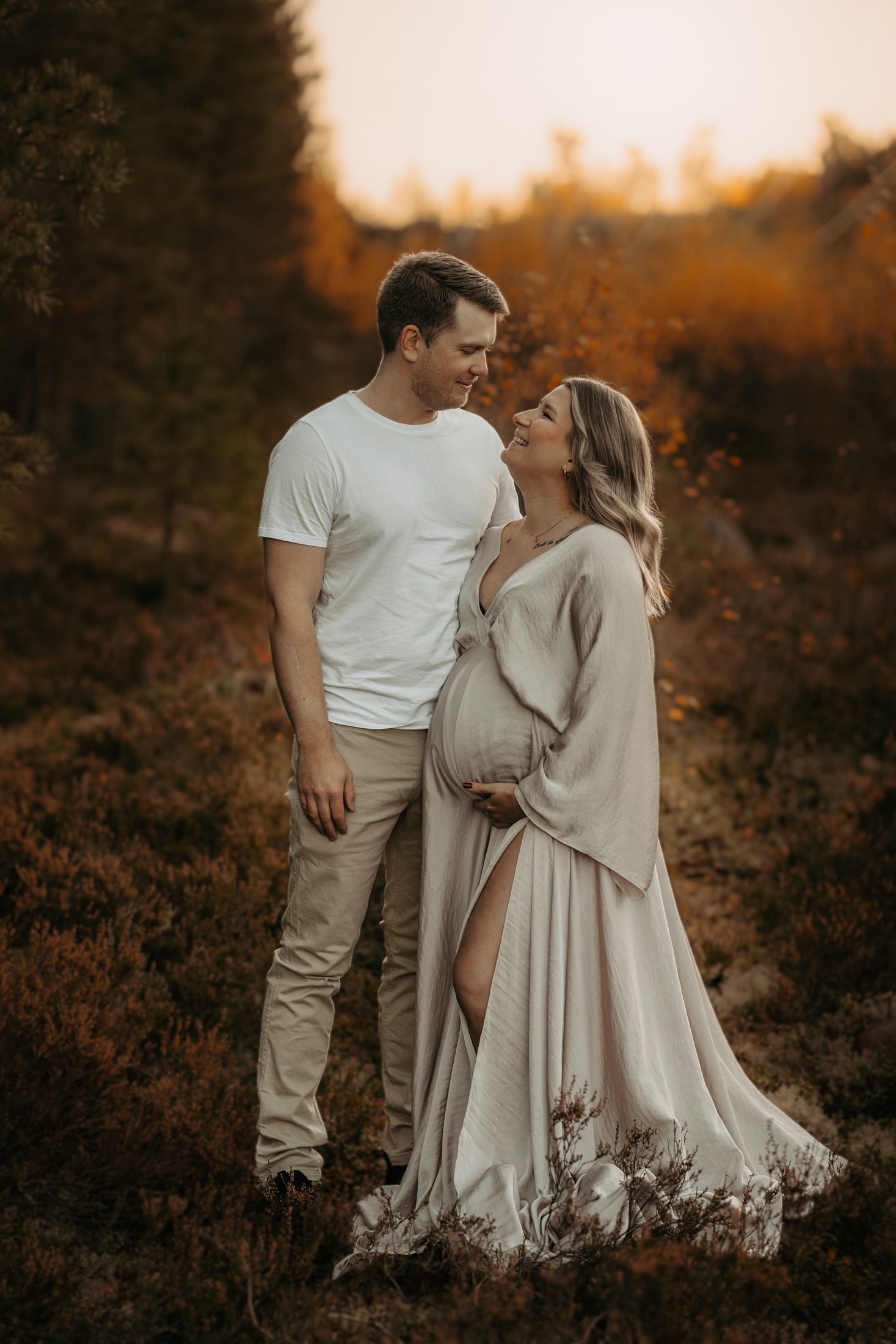 Intimate maternity portrait of couple embracing in golden sunset light among fall foliage.