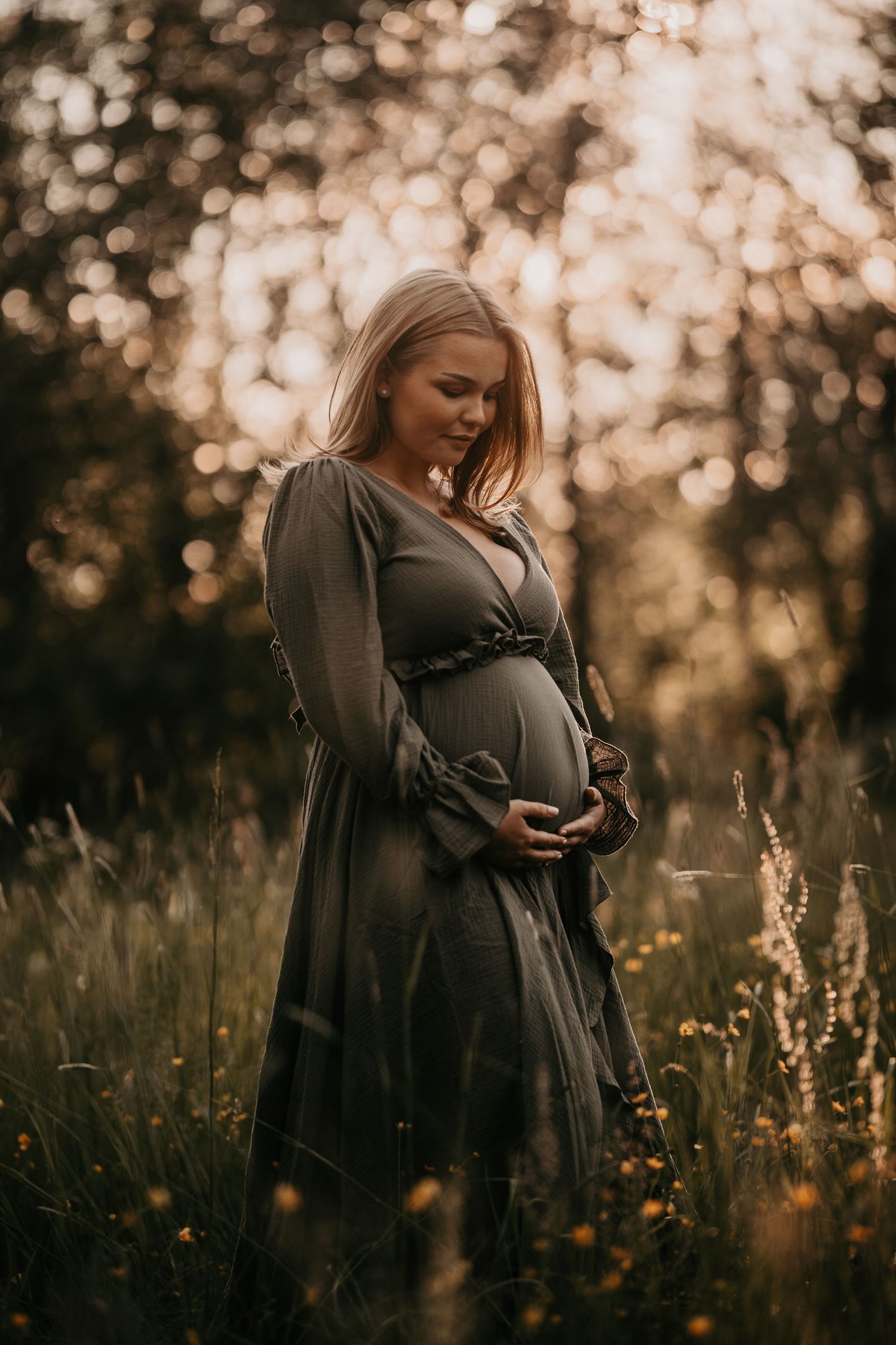Moody maternity portrait in dark dress among wildflowers at golden hour.