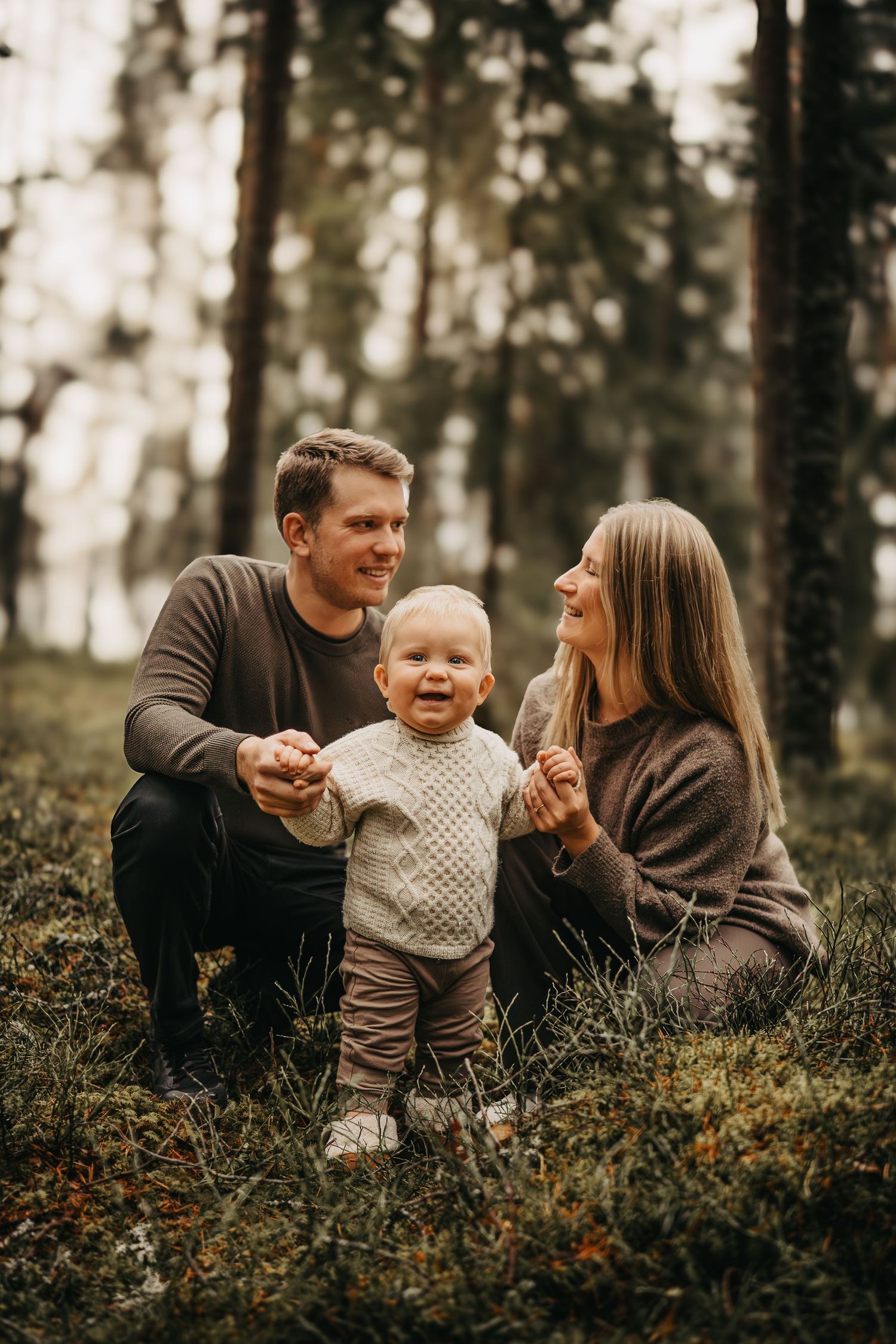 A family of three shares joyful moments together while sitting in a misty forest setting.