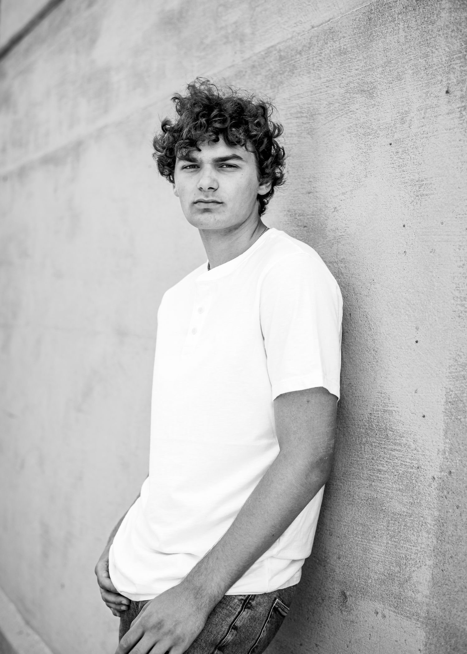 Black and white portrait against textured wall showing casual style in white t-shirt.