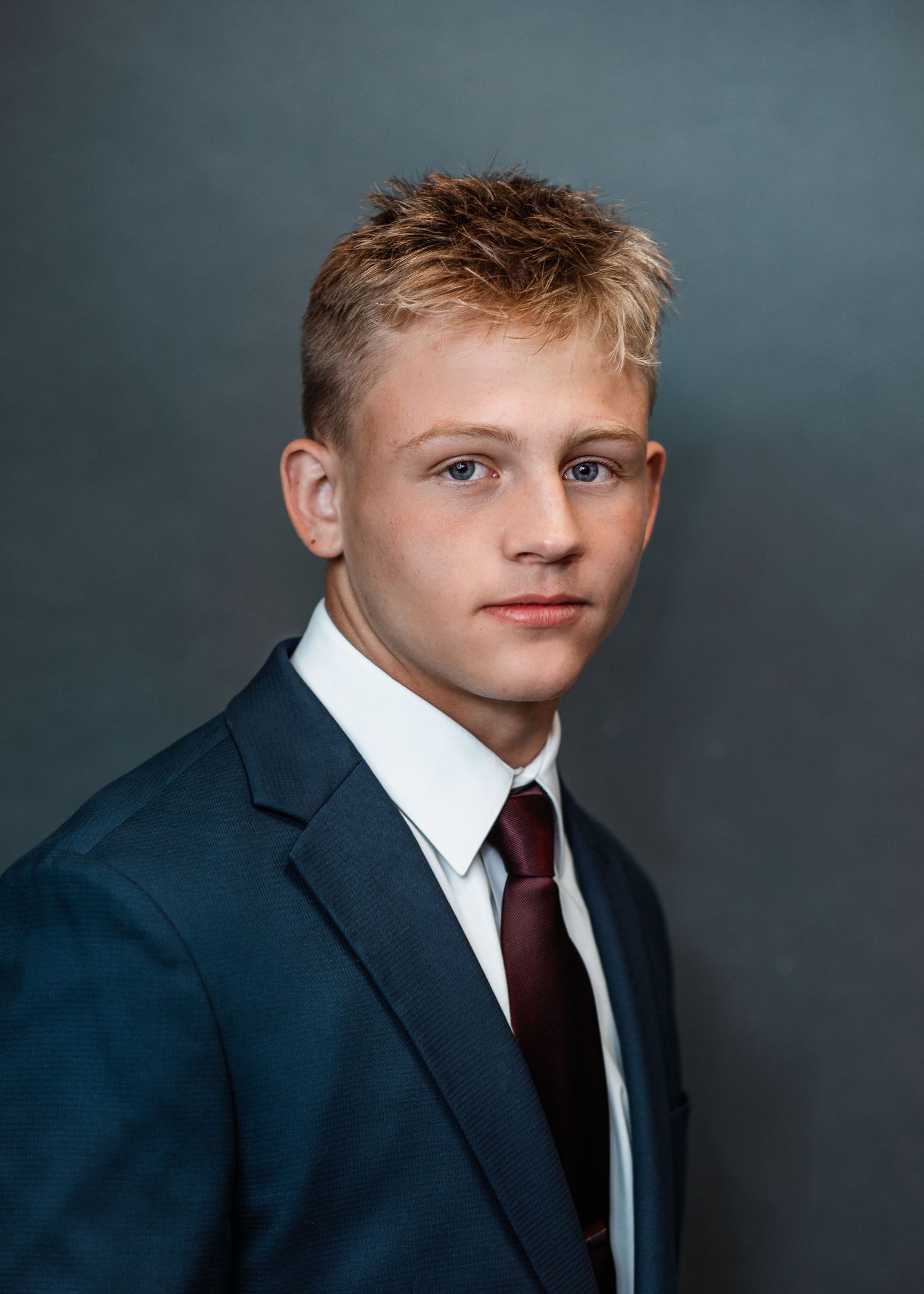 Professional studio portrait of a person in a navy suit and burgundy tie against a gray background.