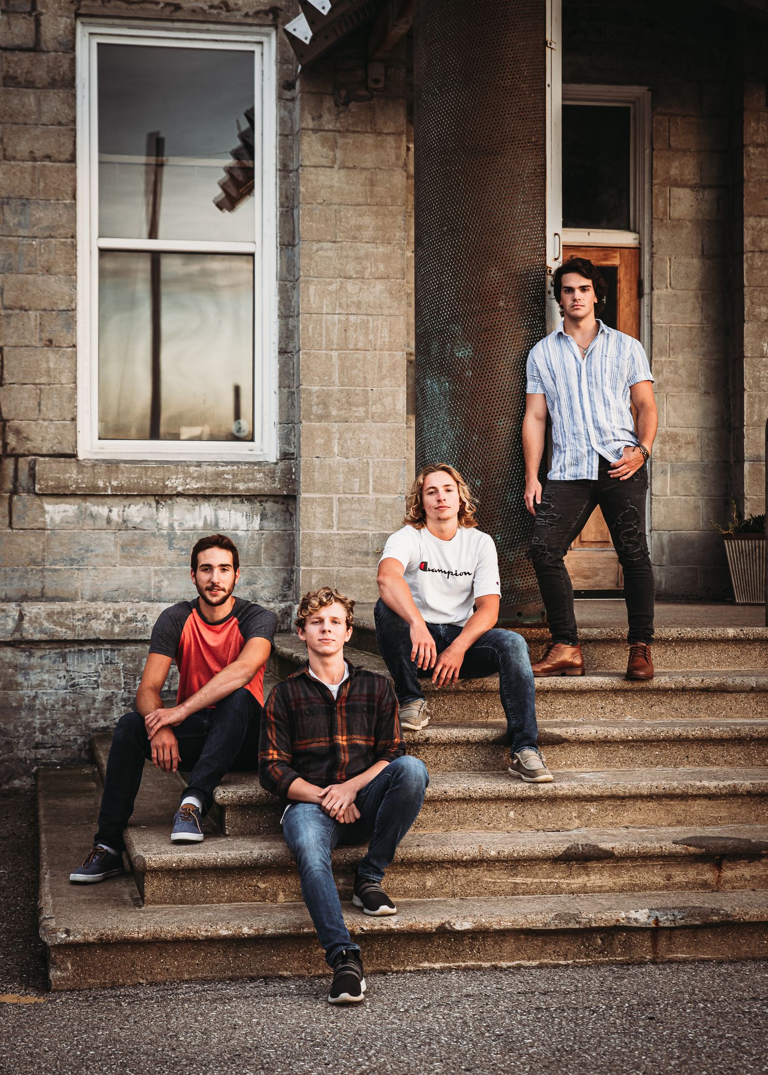 Group sitting on concrete steps outside a brick building with vintage architectural features.