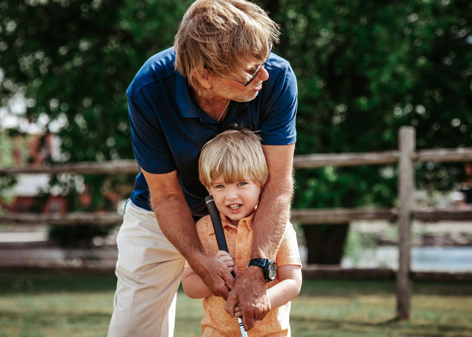 Playful outdoor moment between parent and child in blue shirts against wooden fence.
