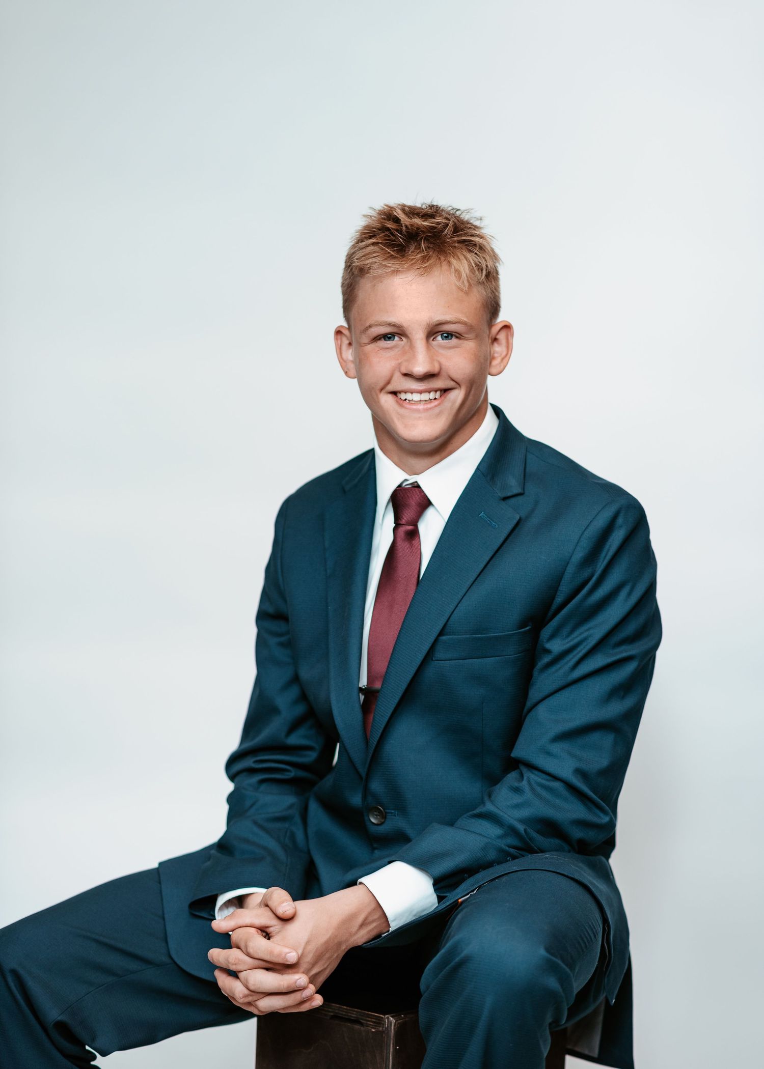 Professional portrait of student in navy suit and red tie against white background.