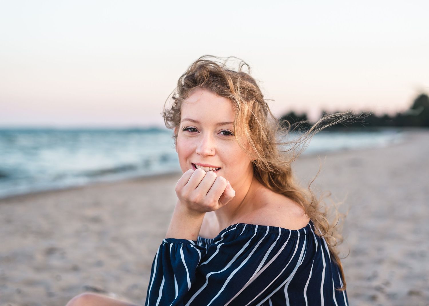 Candid beach portrait at sunset wearing navy striped off-shoulder top.