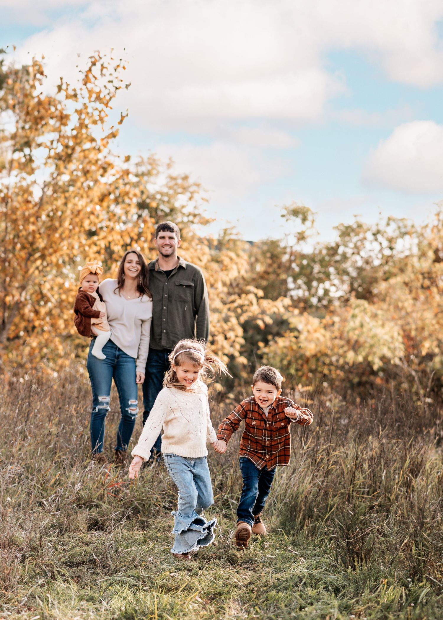 Family enjoying an autumn day in a field with golden grass and trees.