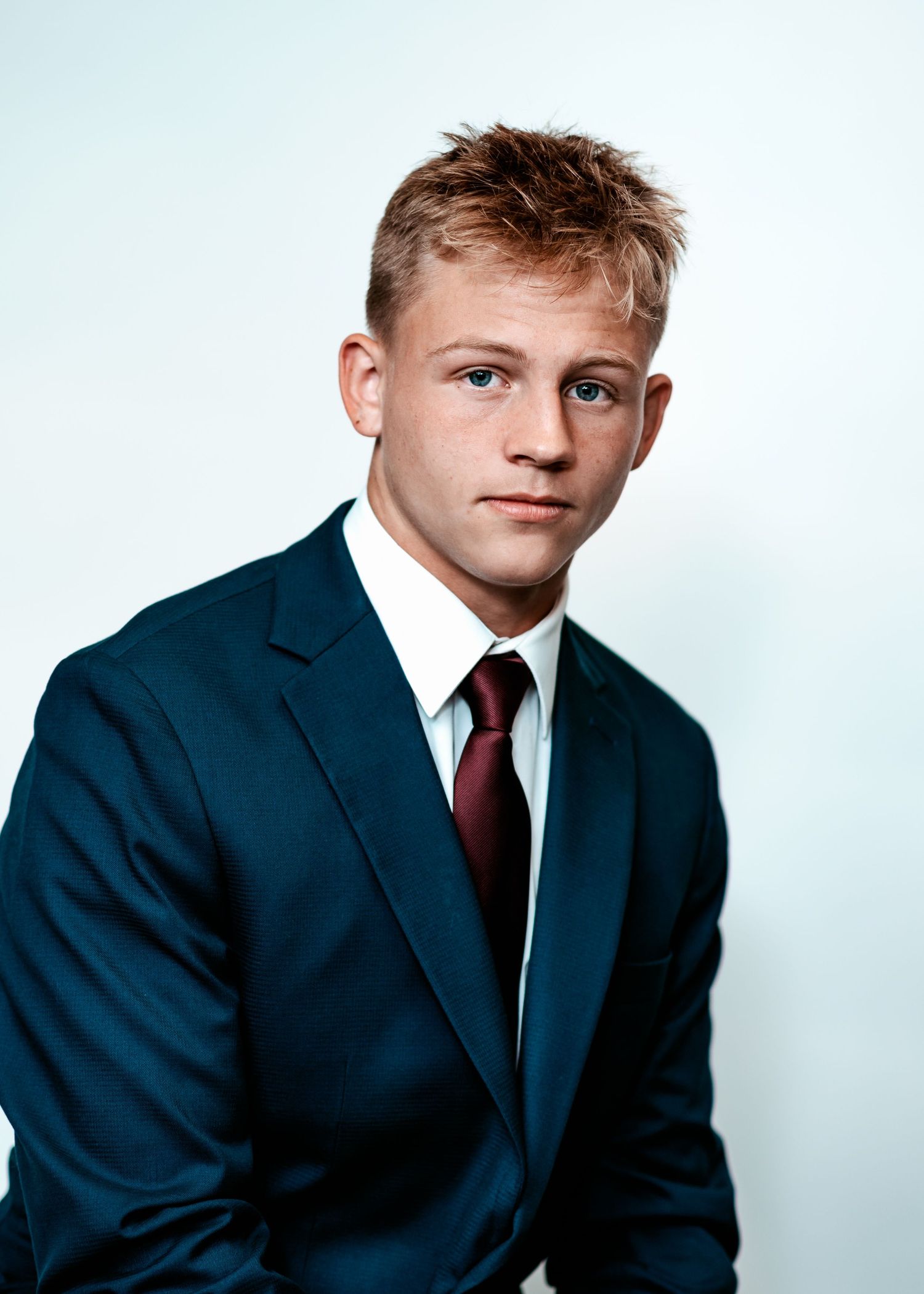 Formal headshot of student wearing navy suit with red tie against light backdrop.
