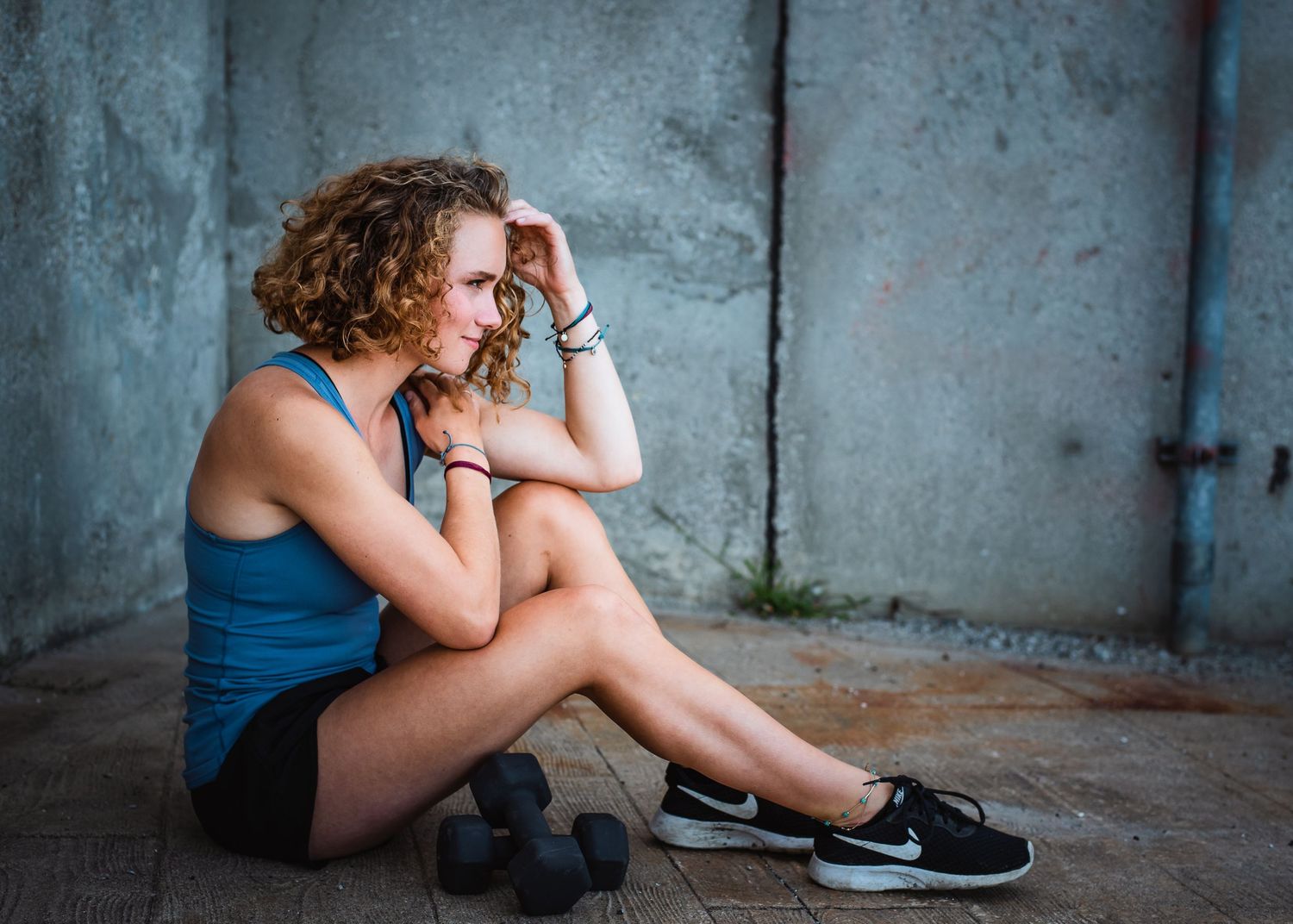 Person in blue tank top sitting on ground against concrete wall with athletic shoes.