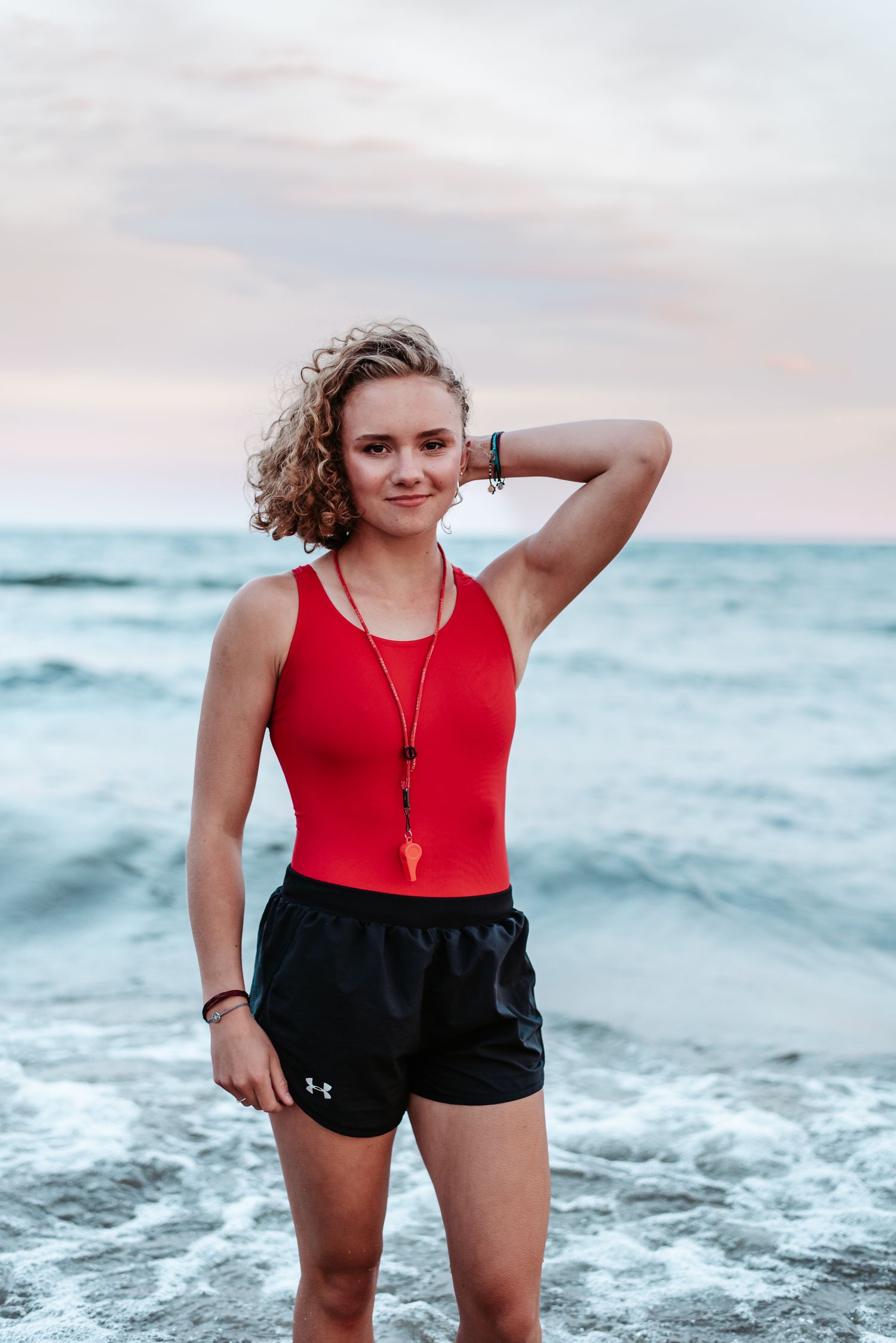 Portrait at beach during sunset with ocean waves and pink sky in background.