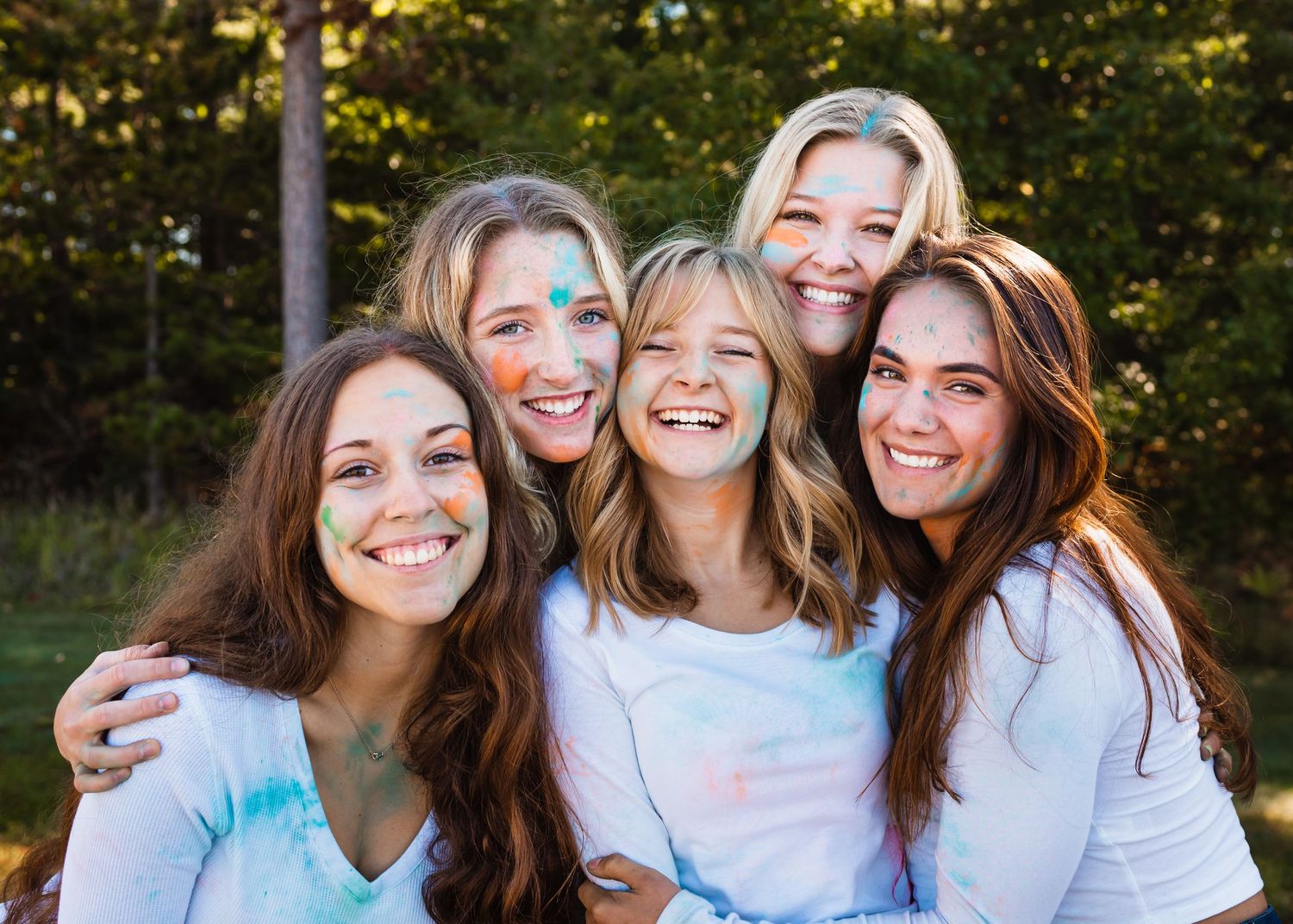 Group of friends in matching white tops with colorful powder during outdoor photo session.