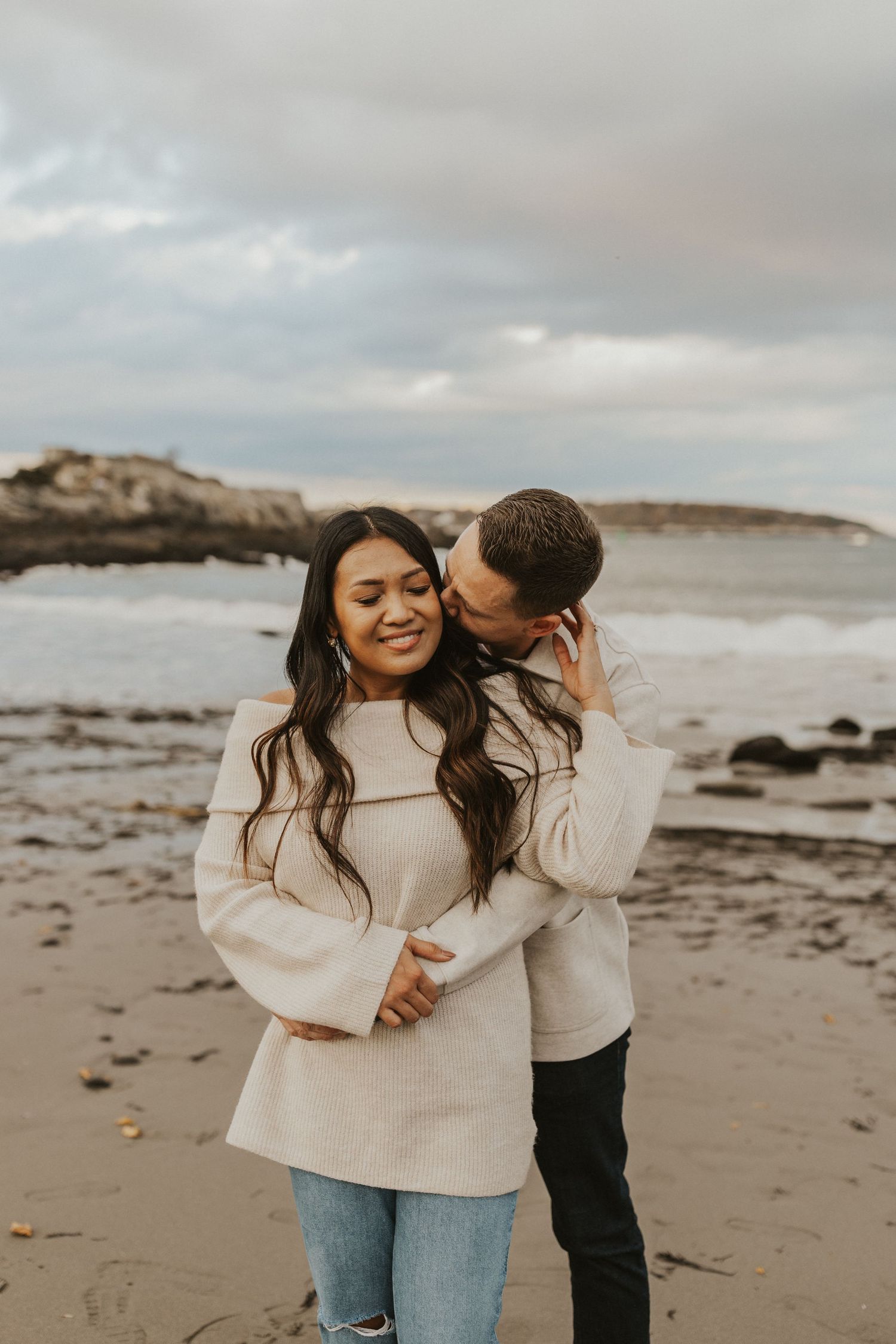 Loving couple shares a tender moment on a rocky beach during sunset.