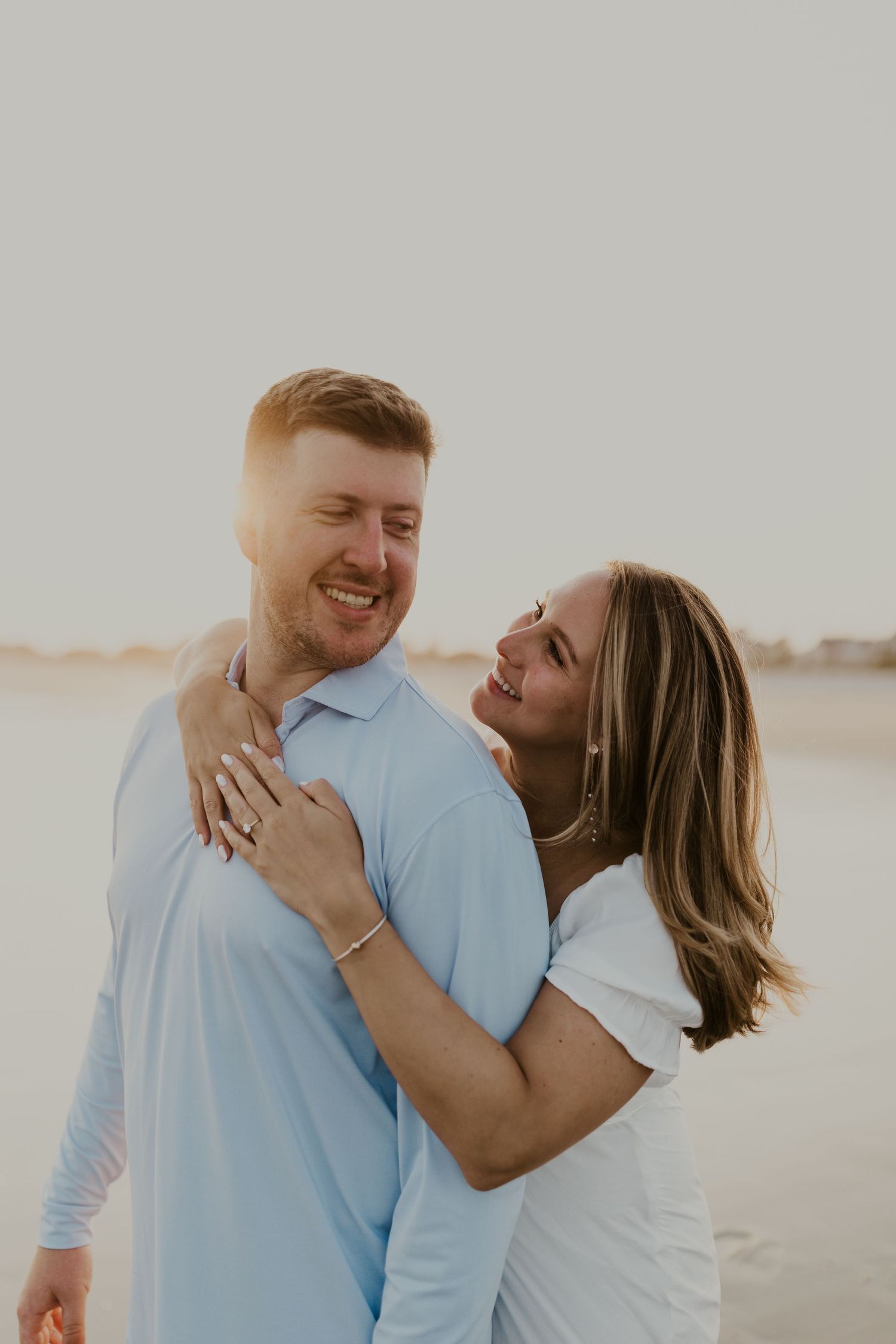 Joyful couple sharing a tender moment on beach at sunset in coordinating blue and white outfits.