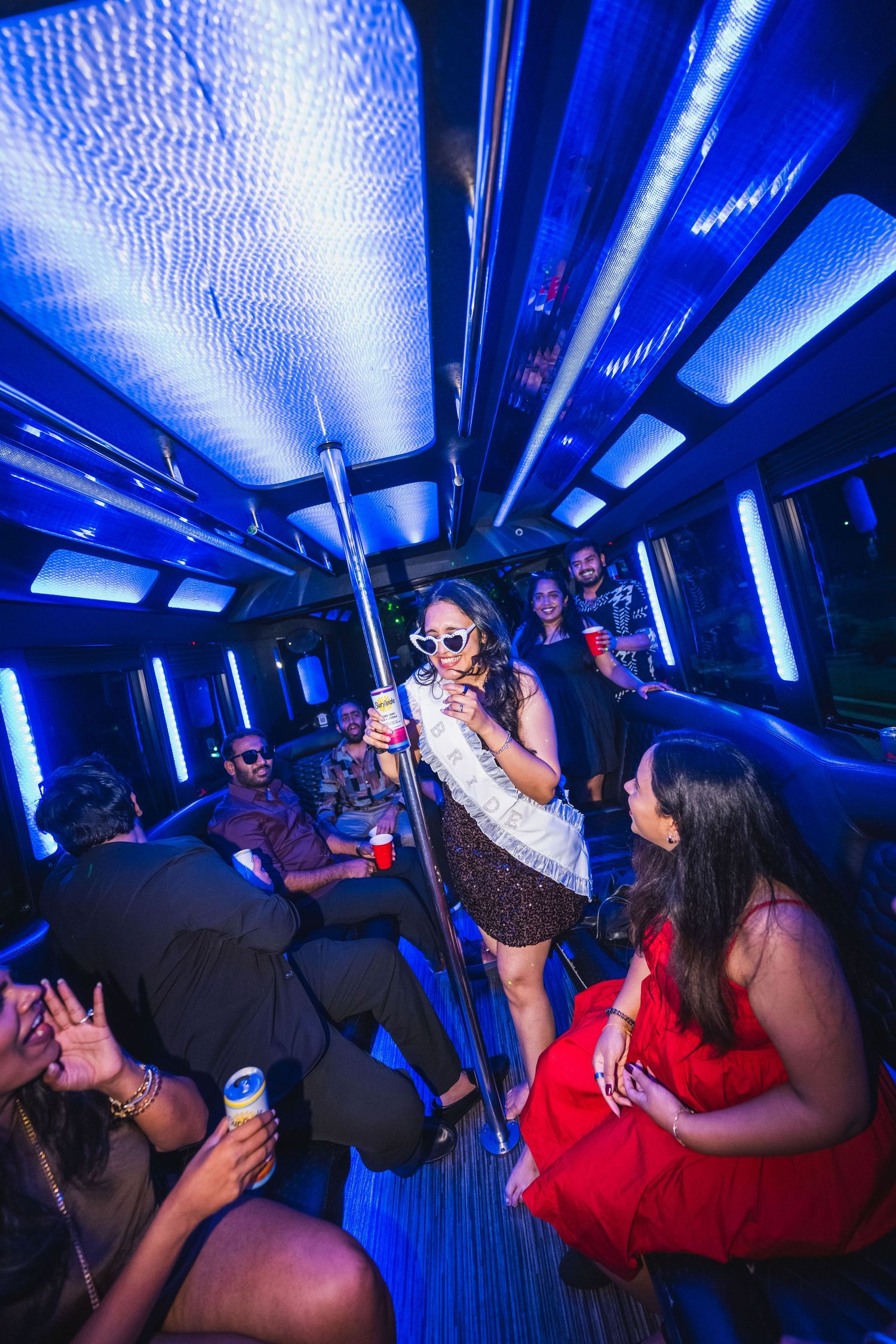 Woman in sparkly dress dancing on party bus with blue neon lights and friends.